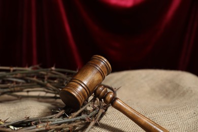Photo of Judge's gavel and crown of thorns on burlap fabric against red curtain, closeup. Space for text