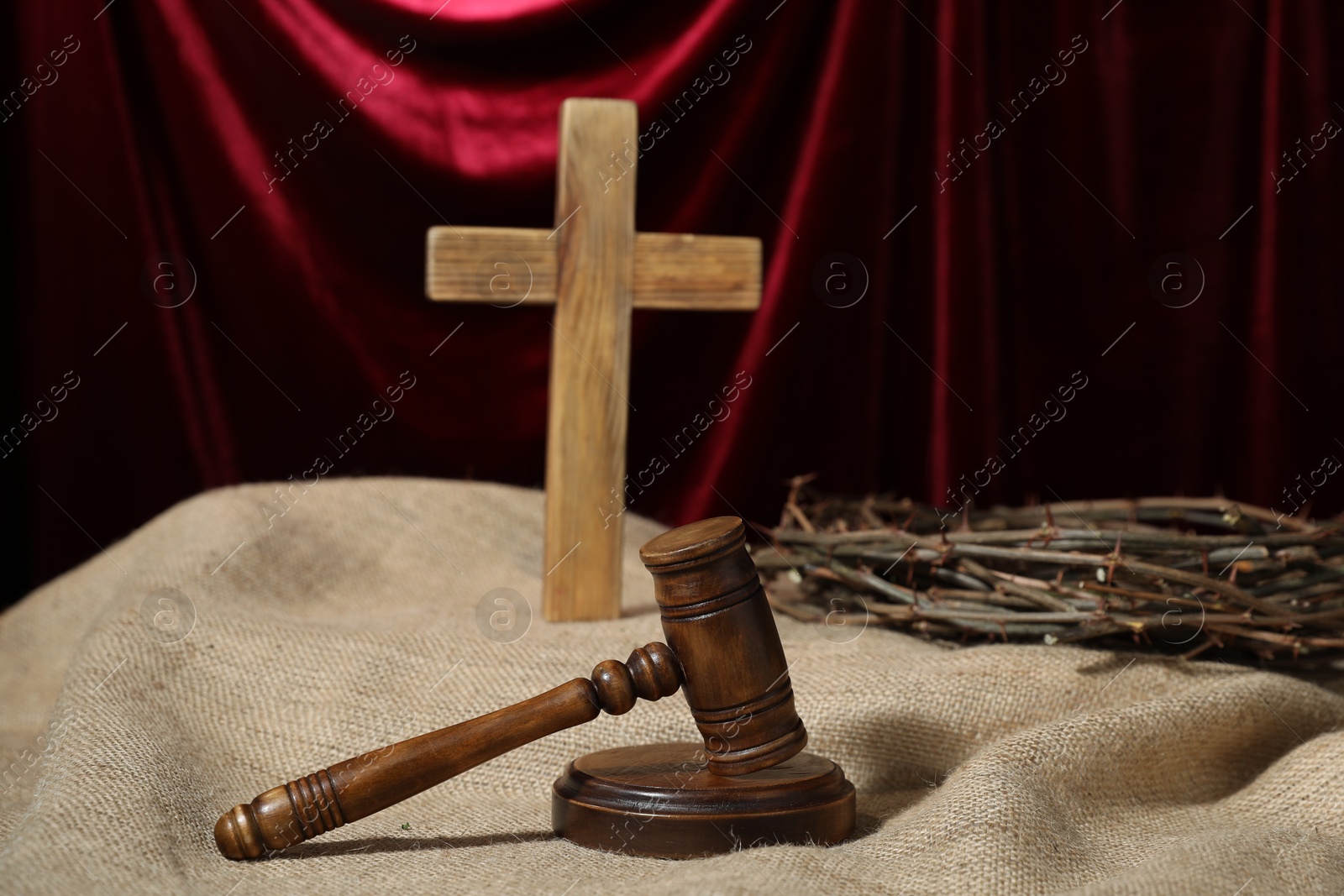 Judge's gavel, wooden cross and crown of thorns on burlap fabric against red curtain Photo of Judge's gavel, wooden cross and crown of thorns on burlap fabric against red curtain