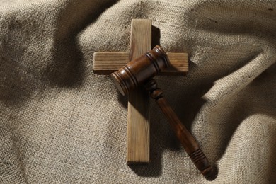 Photo of Judge's gavel and wooden cross on burlap fabric, top view