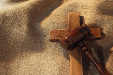 Photo of Judge's gavel and wooden cross on burlap fabric, above view
