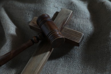 Photo of Judge's gavel and wooden cross on burlap fabric, closeup