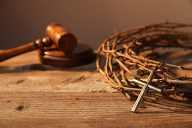 Photo of Crown of thorns with cross and judge's gavel on wooden table, closeup