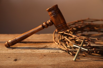 Photo of Judge's gavel, crown of thorns and cross on wooden table, closeup