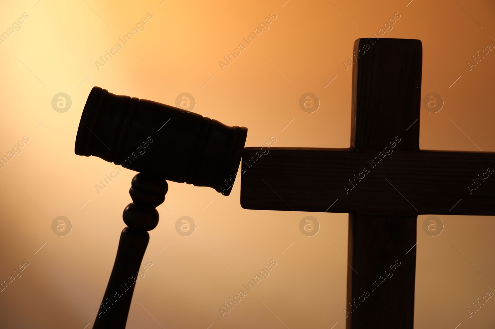 Silhouette of judge's gavel and cross on pale orange gradient background, closeup Photo of Silhouette of judge's gavel and cross on pale orange gradient background, closeup