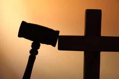 Photo of Silhouette of judge's gavel and cross on pale orange gradient background, closeup