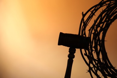 Photo of Silhouette of judge's gavel and crown of thorns on pale orange gradient background, closeup. Space for text
