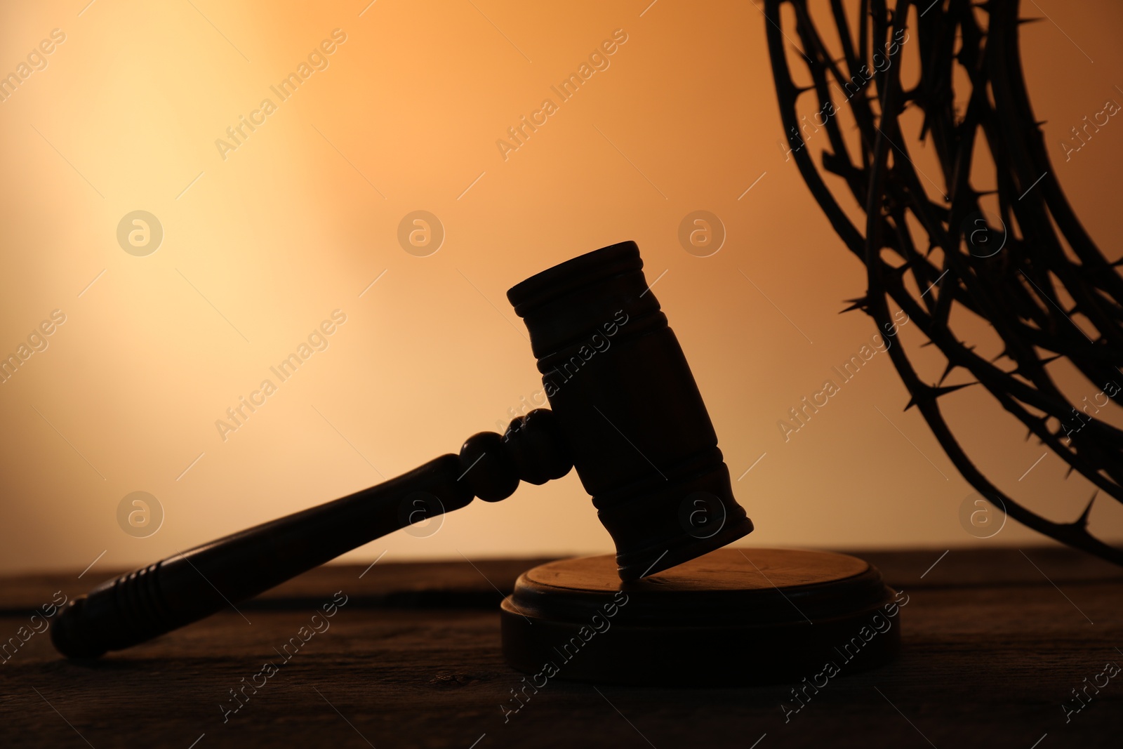Silhouette of judge's gavel and crown of thorns on wooden table against pale orange gradient background, closeup Photo of Silhouette of judge's gavel and crown of thorns on wooden table against pale orange gradient background, closeup