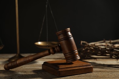Photo of Judge's gavel, scales and crown of thorns on wooden table against black background, closeup