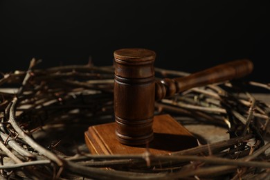 Photo of Judge's gavel and crown of thorns on table against black background, closeup