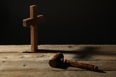 Photo of Judge's gavel and cross on wooden table against black background