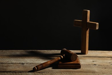 Photo of Judge's gavel and cross on wooden table against black background