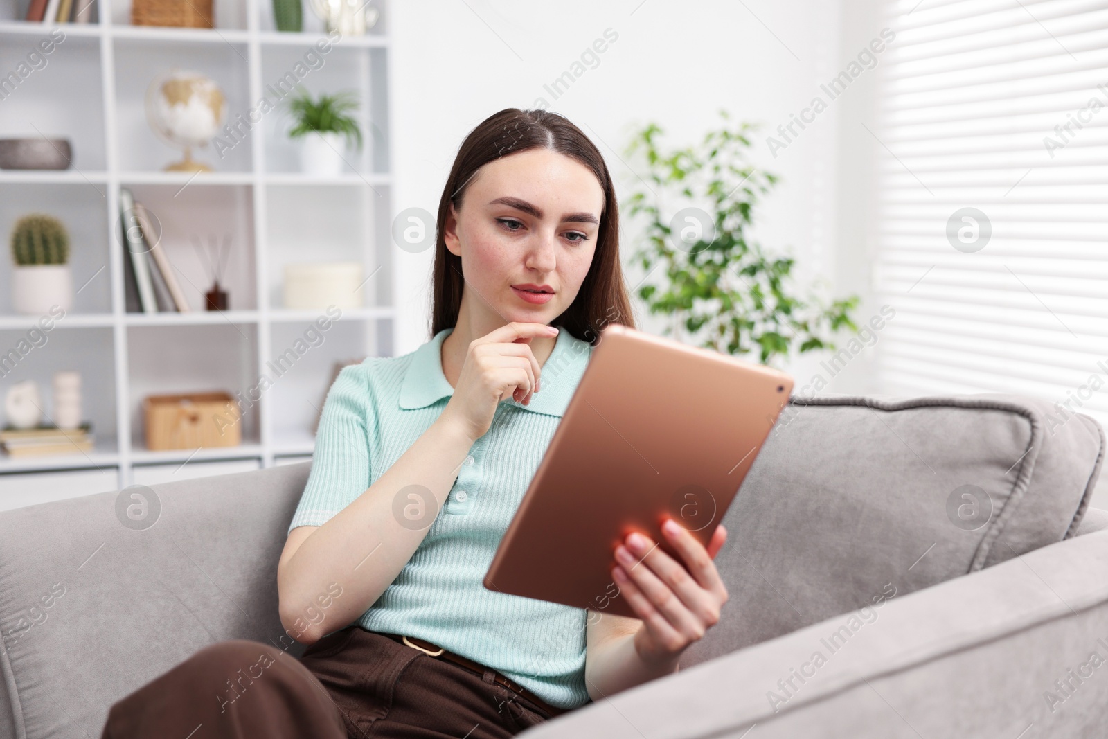 Young woman using modern tablet in armchair at home Photo of Young woman using modern tablet in armchair at home