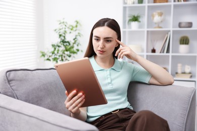Photo of Young woman using modern tablet in armchair at home