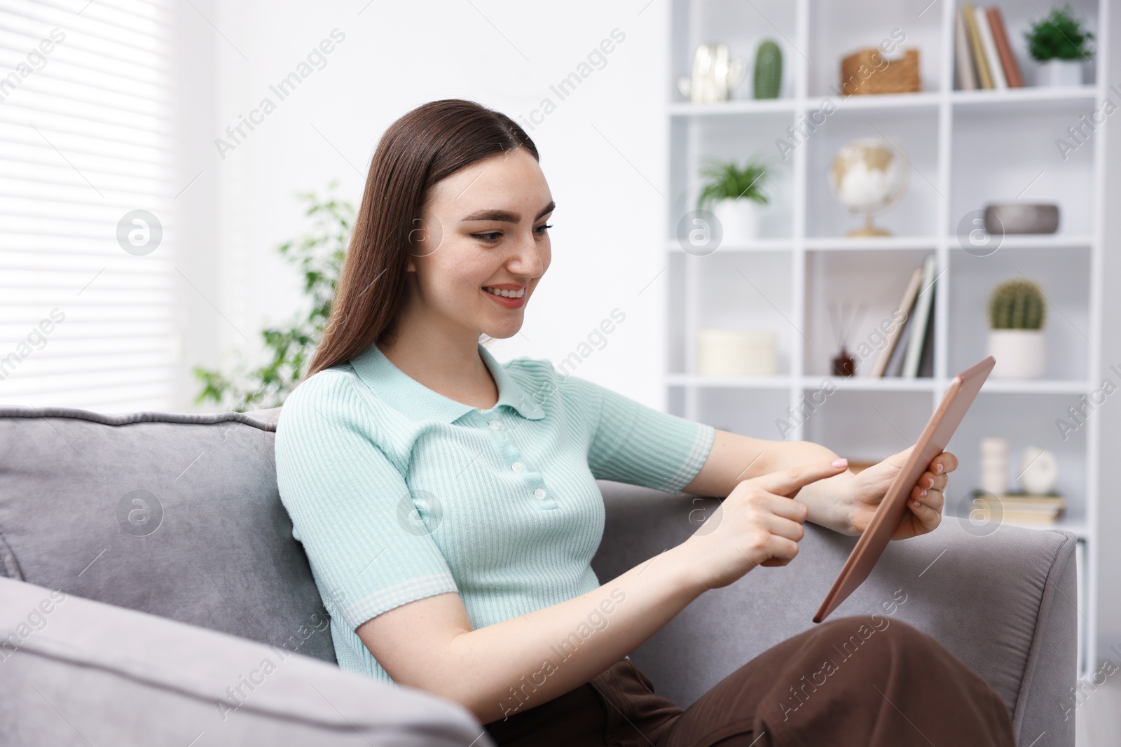 Young woman using modern tablet in armchair at home Photo of Young woman using modern tablet in armchair at home