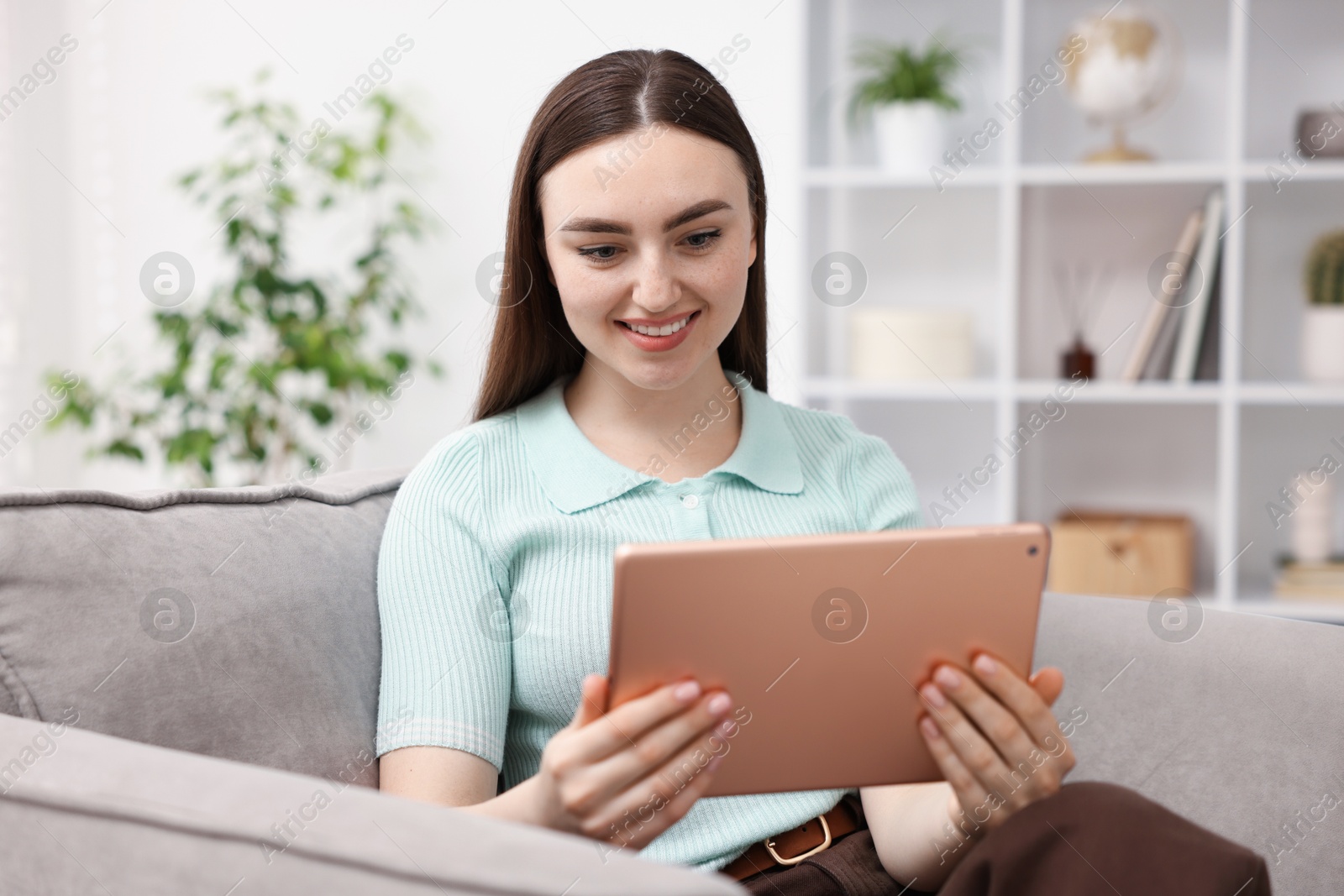 Young woman using modern tablet in armchair at home Photo of Young woman using modern tablet in armchair at home