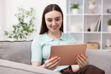Photo of Young woman using modern tablet in armchair at home