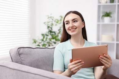 Photo of Young woman using modern tablet in armchair at home. Space for text