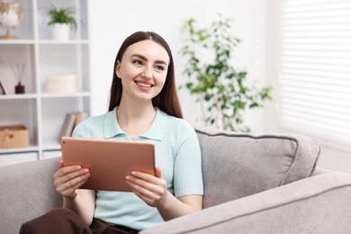 Photo of Young woman using modern tablet in armchair at home. Space for text