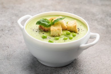 Photo of Tasty pea cream soup with croutons and basil on grey table, closeup