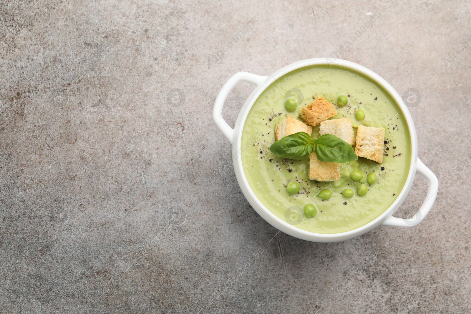 Tasty pea cream soup with croutons and basil on grey table, top view. Space for text Photo of Tasty pea cream soup with croutons and basil on grey table, top view. Space for text