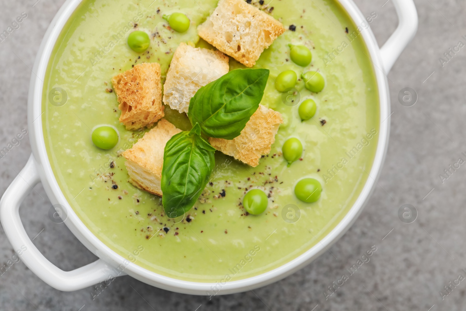 Tasty pea cream soup with croutons and basil on grey table, top view Photo of Tasty pea cream soup with croutons and basil on grey table, top view