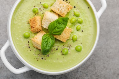 Photo of Tasty pea cream soup with croutons and basil on grey table, top view