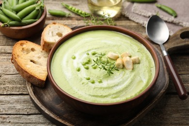 Photo of Tasty pea cream soup with croutons and thyme served on wooden table, closeup