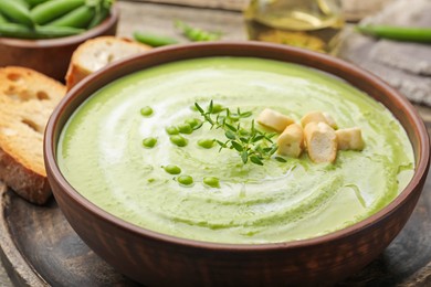 Photo of Tasty pea cream soup with croutons and thyme served on wooden table, closeup