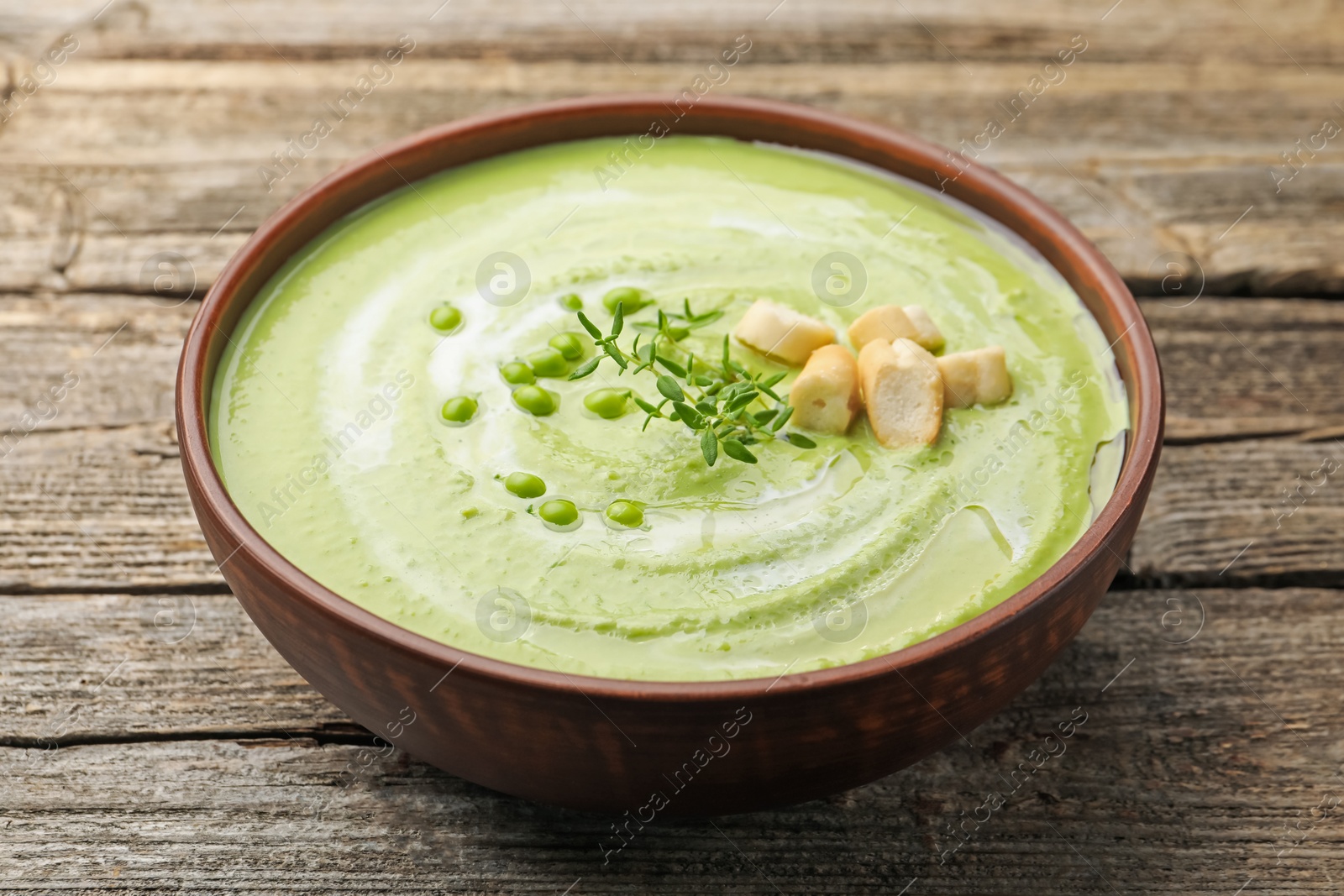 Tasty pea cream soup with croutons and thyme on wooden table, closeup Photo of Tasty pea cream soup with croutons and thyme on wooden table, closeup