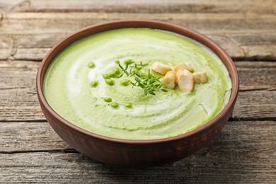 Photo of Tasty pea cream soup with croutons and thyme on wooden table, closeup
