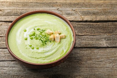 Photo of Tasty pea cream soup with croutons and thyme on wooden table, closeup. Space for text