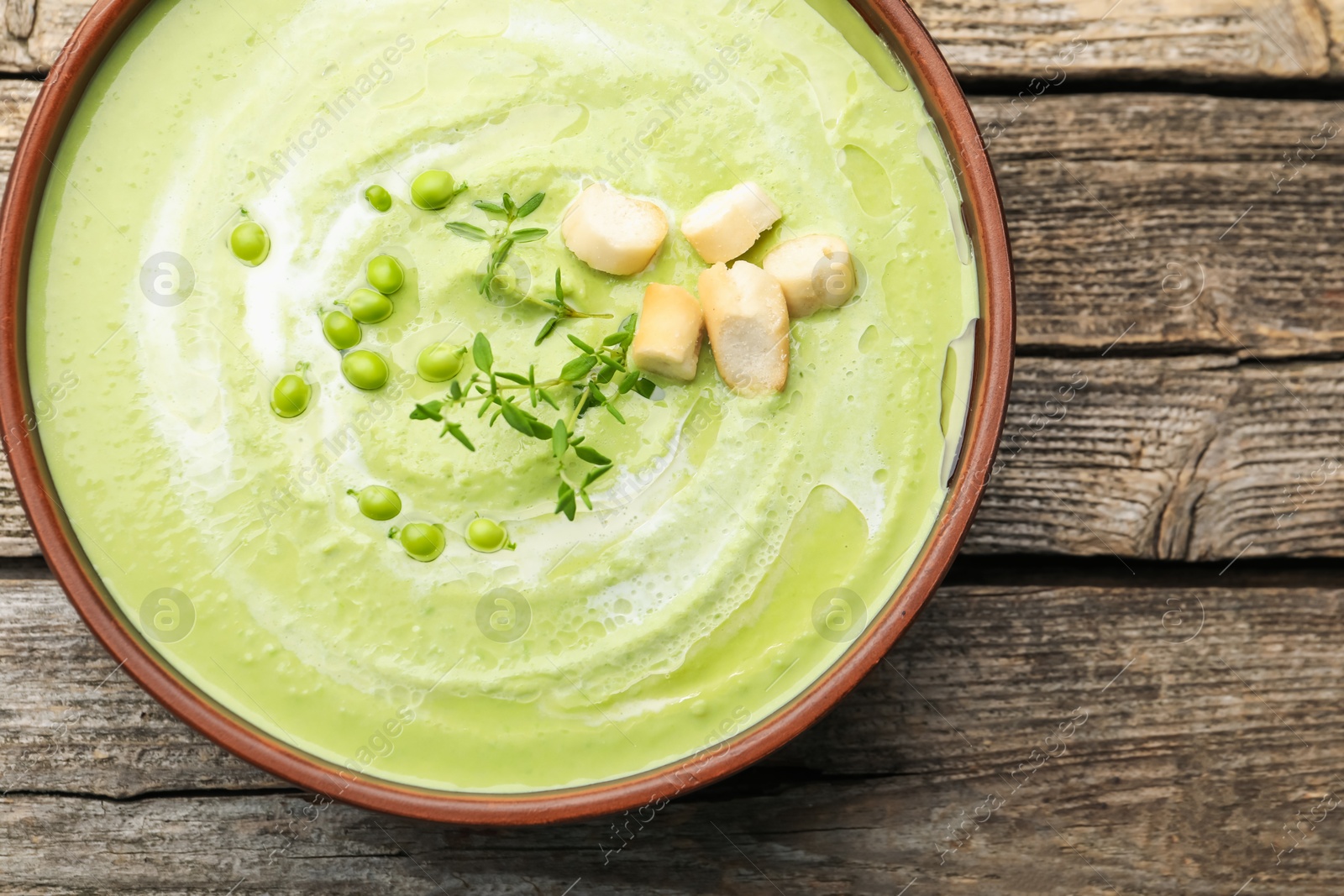Tasty pea cream soup with croutons and thyme on wooden table, top view Photo of Tasty pea cream soup with croutons and thyme on wooden table, top view