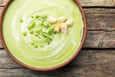 Photo of Tasty pea cream soup with croutons and thyme on wooden table, top view