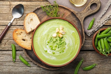 Photo of Tasty pea cream soup with croutons and thyme served on wooden table, flat lay
