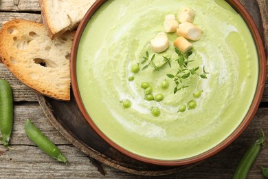 Photo of Tasty pea cream soup with croutons and thyme served on wooden table, flat lay