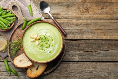 Photo of Tasty pea cream soup with croutons and thyme served on wooden table, flat lay. Space for text