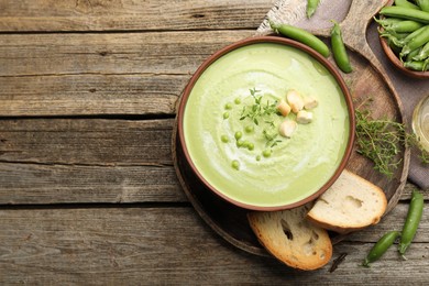 Photo of Tasty pea cream soup with croutons and thyme served on wooden table, flat lay. Space for text