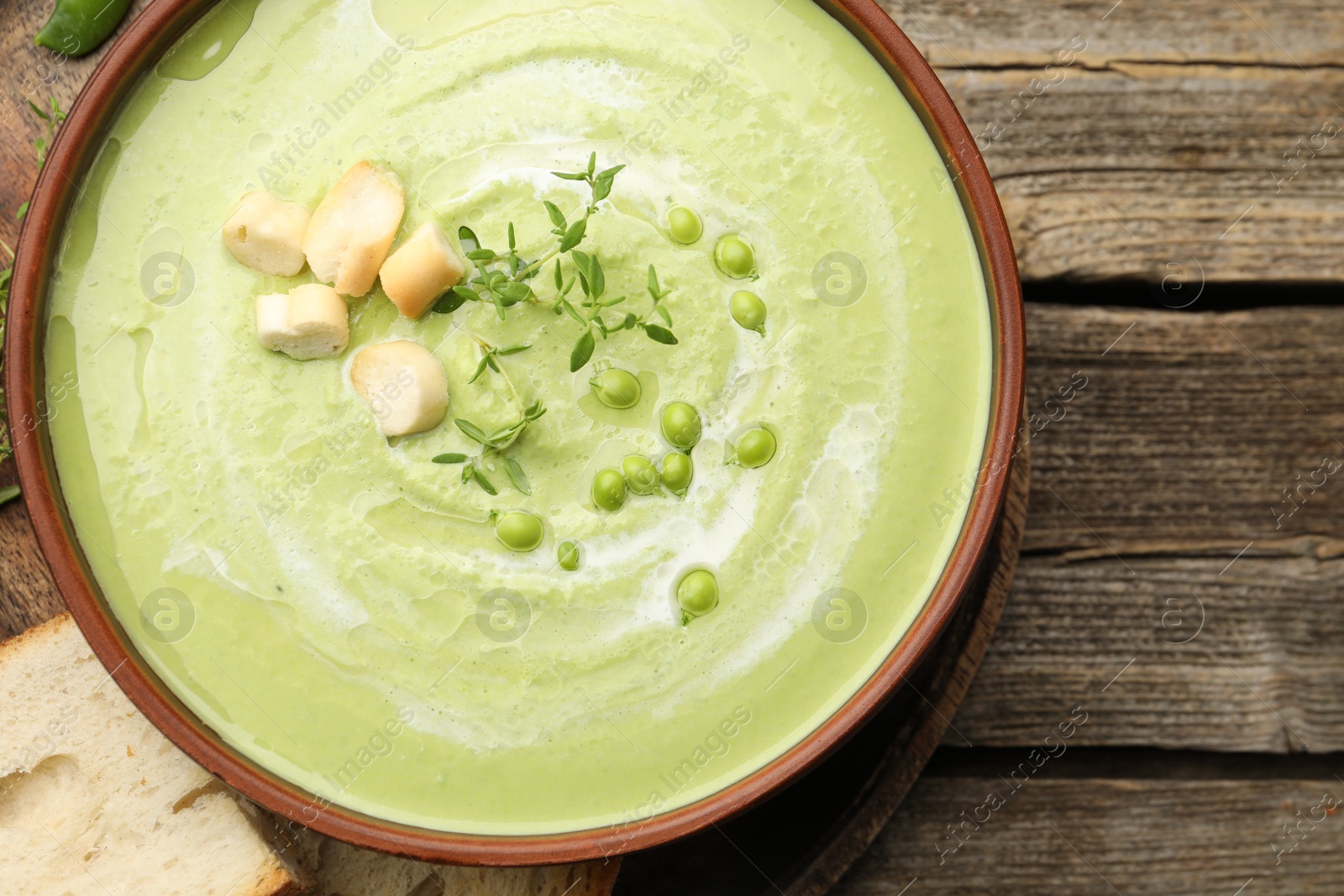 Tasty pea cream soup with croutons and thyme served on wooden table, top view Photo of Tasty pea cream soup with croutons and thyme served on wooden table, top view