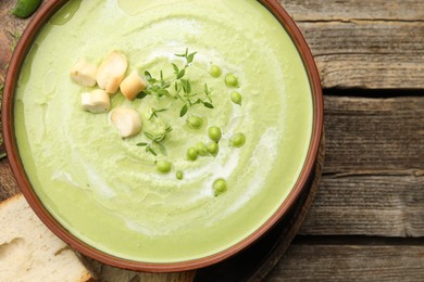 Photo of Tasty pea cream soup with croutons and thyme served on wooden table, top view