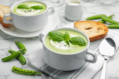Photo of Tasty pea cream soup with basil served on white marble table