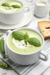 Photo of Tasty pea cream soup with basil served on white table