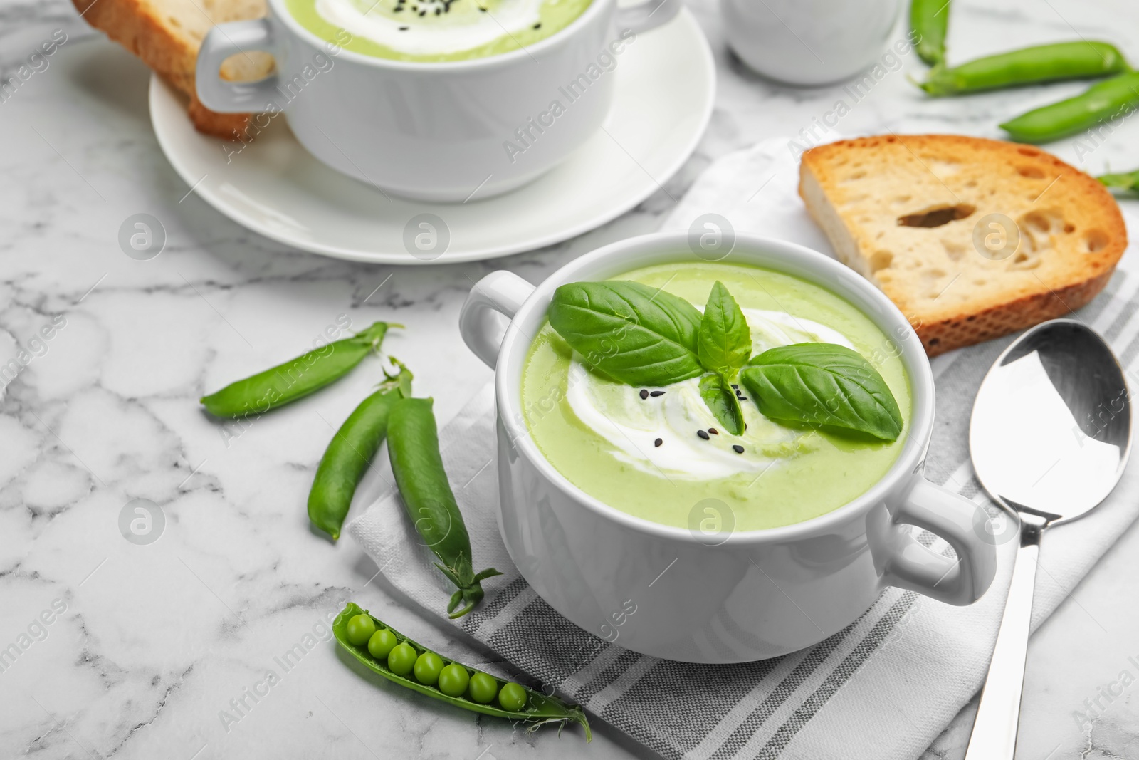 Tasty pea cream soup with basil served on white marble table Photo of Tasty pea cream soup with basil served on white marble table
