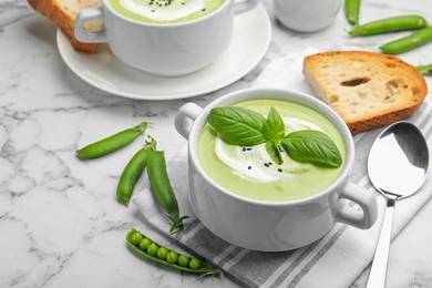 Photo of Tasty pea cream soup with basil served on white marble table