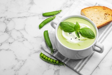 Photo of Tasty pea cream soup with basil served on white marble table. Space for text
