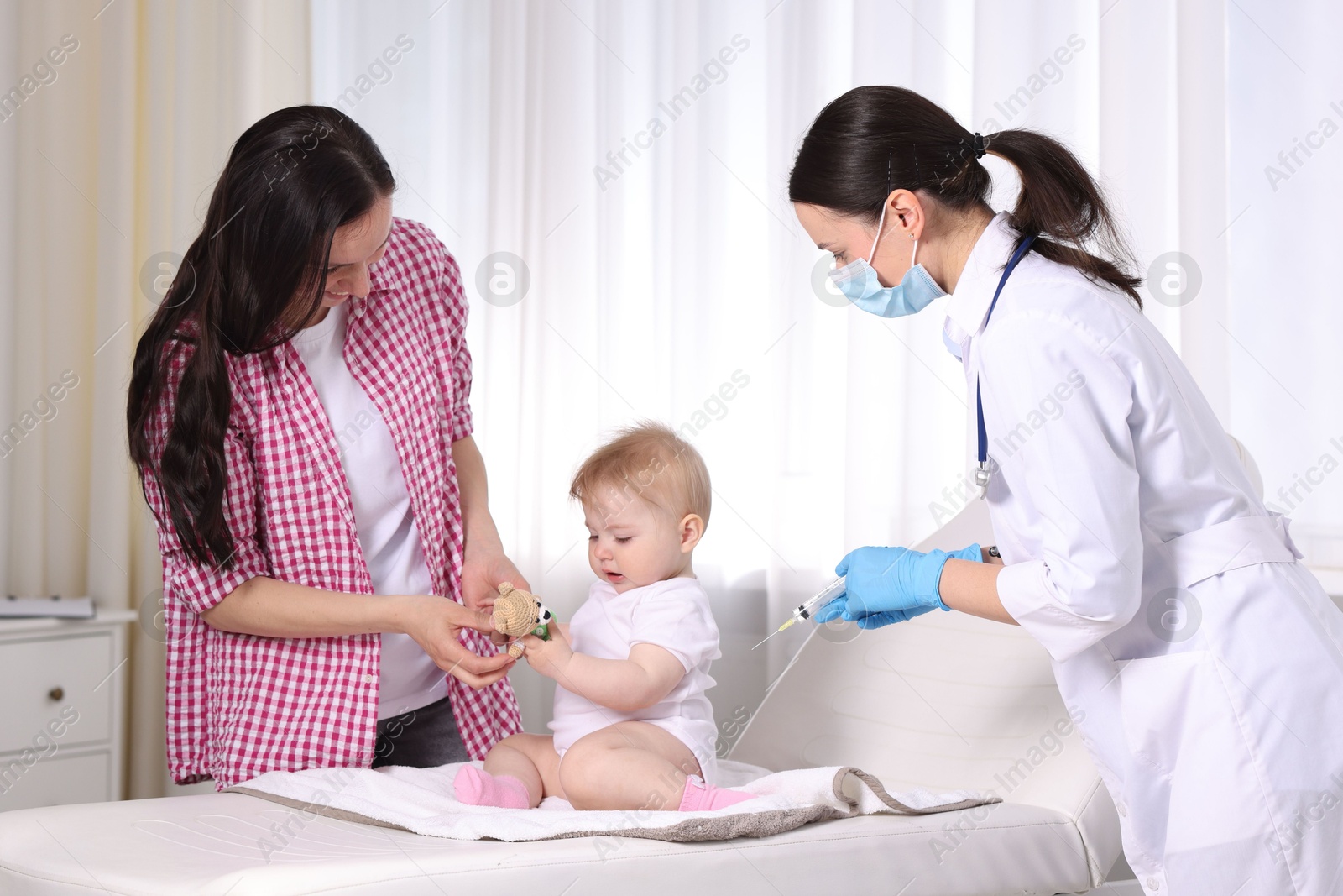 Mother and her cute baby having appointment with pediatrician in clinic. Doctor vaccinating child Photo of Mother and her cute baby having appointment with pediatrician in clinic. Doctor vaccinating child