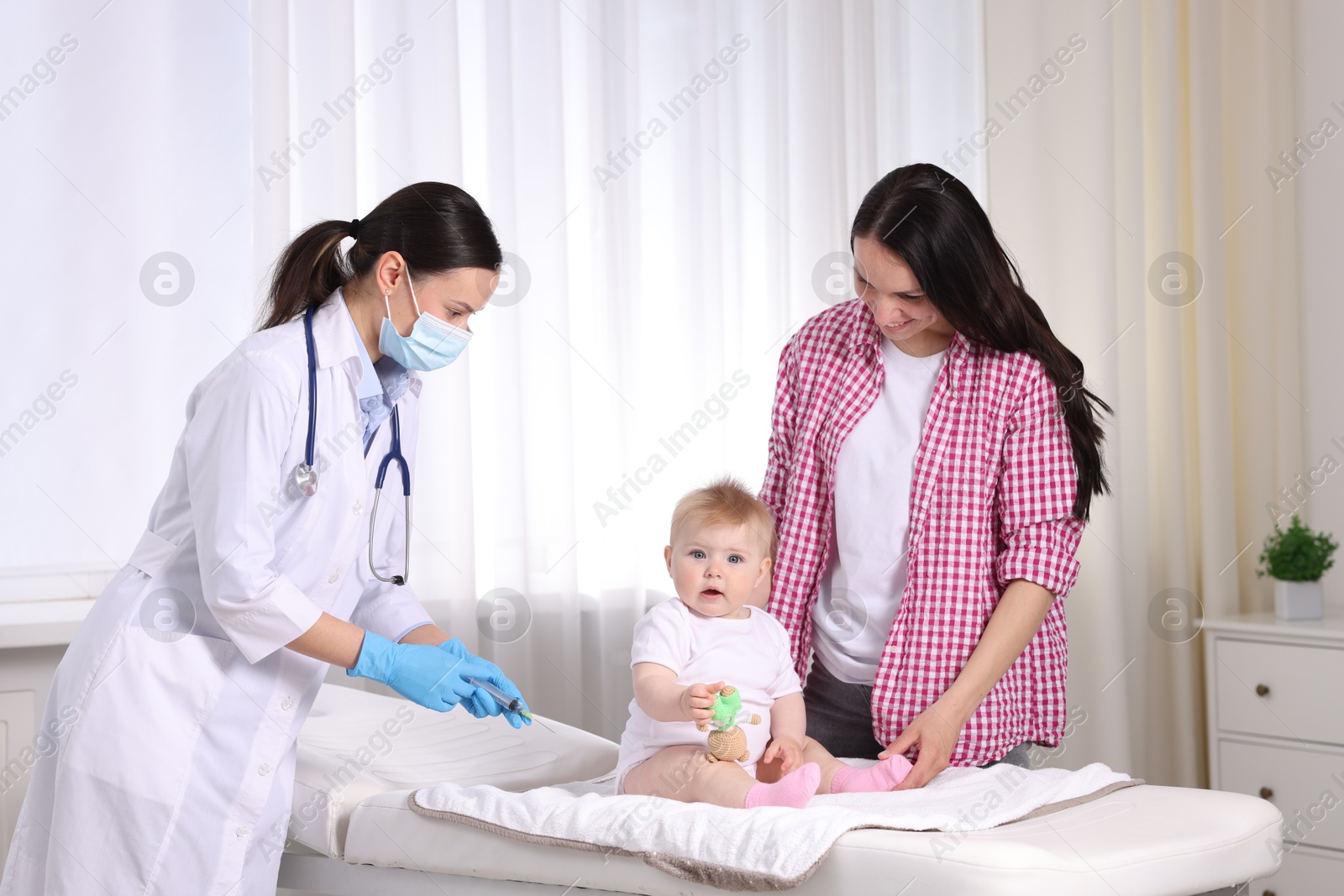 Mother and her cute baby having appointment with pediatrician in clinic. Doctor vaccinating child Photo of Mother and her cute baby having appointment with pediatrician in clinic. Doctor vaccinating child