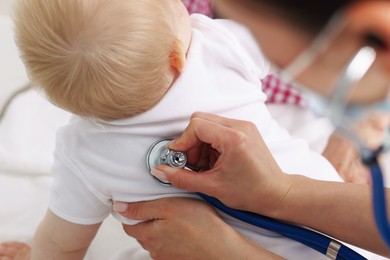 Photo of Pediatrician examining baby with stethoscope in clinic, closeup