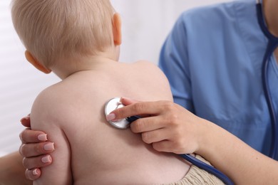 Photo of Pediatrician examining baby with stethoscope in clinic, closeup
