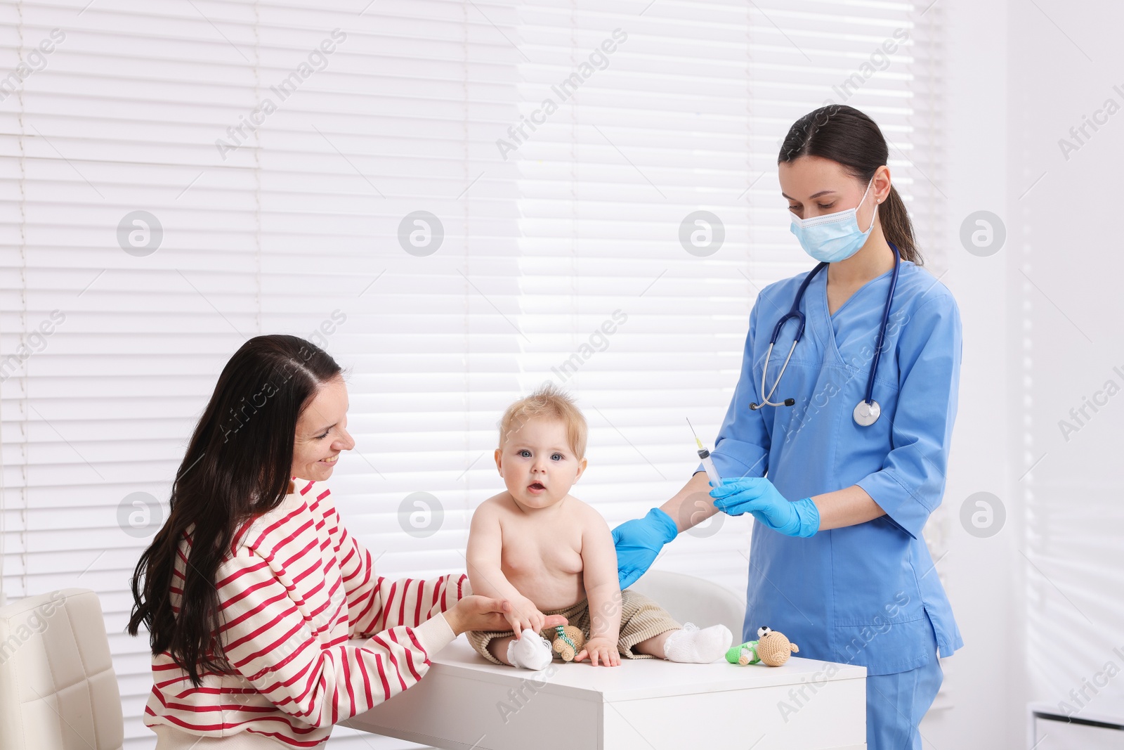 Mother and her cute baby having appointment with pediatrician in clinic. Doctor vaccinating child Photo of Mother and her cute baby having appointment with pediatrician in clinic. Doctor vaccinating child