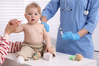 Photo of Mother and her cute baby having appointment with pediatrician in clinic, closeup. Doctor vaccinating child